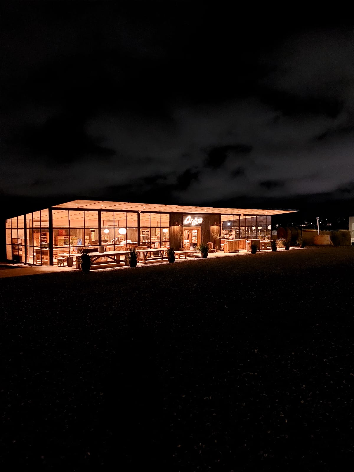 El local de Origen iluminado de noche, con amplios ventanales y muebles en exhibición